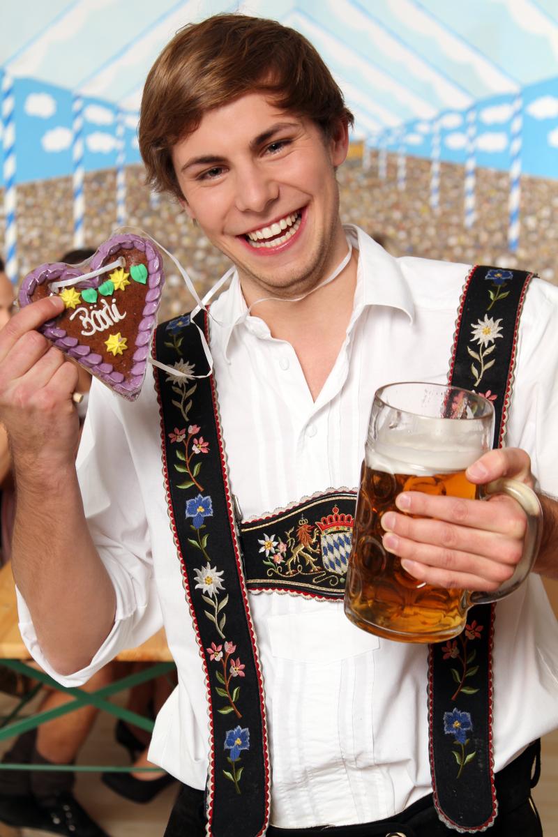 Young man in a bavarian costume with a beer bug and a chocolate heart in the hand  